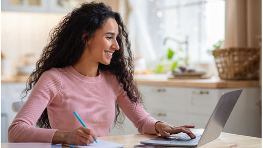 woman in front of laptop at kitchen table working on her alternative certification program for education prep